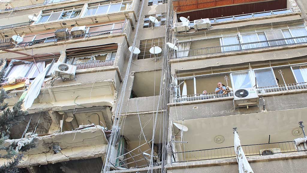 People stand on a balcony of a damaged building in the aftermath of what Syrian state media reported was an Israeli strike in the Mezzah suburb west of Damascus, Syria Oct 9, 2024. REUTERS/Firas Makdesi