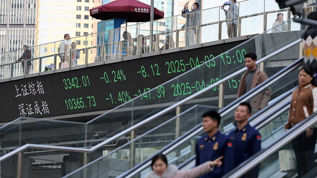 FILE PHOTO: An electronic board shows Shanghai and Shenzhen stock indices as people walk on a pedestrian bridge at the Lujiazui financial district in Shanghai, China Apr 3, 2025. REUTERS/Go Nakamura/File Photo/File Photo