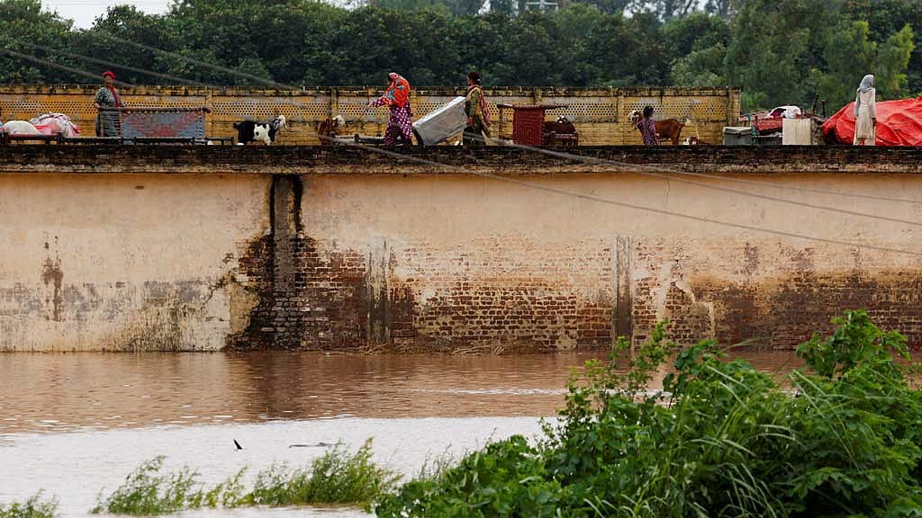 A family with their belongings takes refuge over a roof of their house near Chenab River, following the monsoon rains and rising water level in Wazirabad, in Punjab province, Pakistan Aug 27, 2025. REUTERS/Akhtar Soomro
