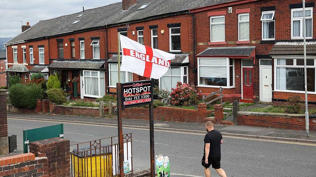  A man walks past a flag bearing the colours of England's St. George's Cross, flying above a residential street in Radcliffe, near Manchester, Britain, Aug 22, 2025. REUTERS/Temilade Adelaja