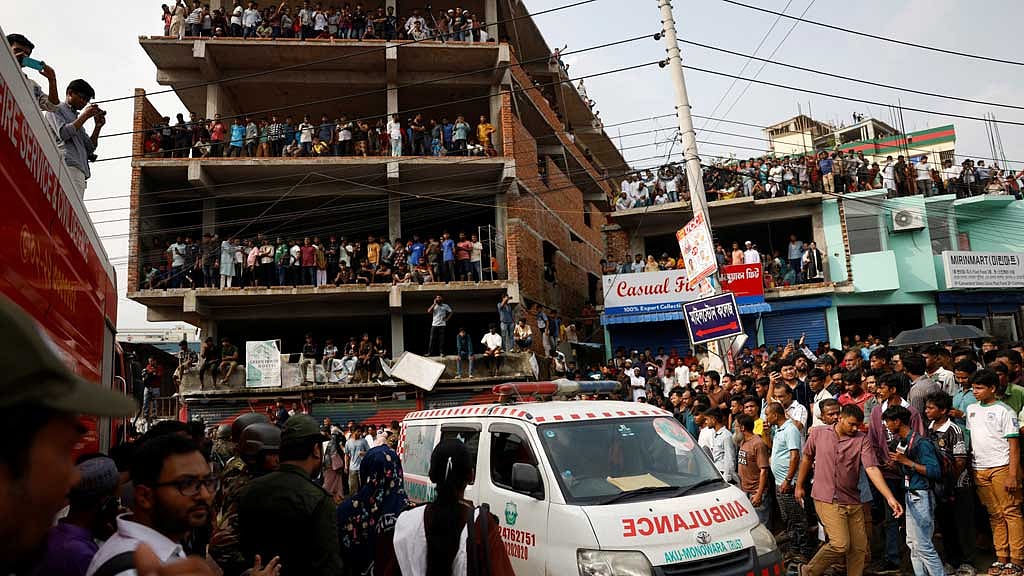 A passenger airplane flies as onlookers watch a rescue operation after an air force training aircraft crashed into Milestone College campus, in Dhaka, Jul 21, 2025. REUTERS/Mohammad Ponir Hossain