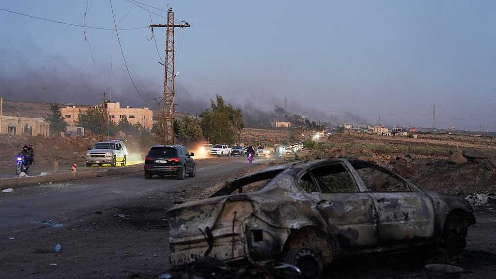 Smoke rises as a damaged car remains along a street, as Sweida province has been engulfed by nearly a week of violence triggered by clashes between Bedouin fighters and factions from the Druze, at Sweida governorate, Syria, July 18, 2025. REUTERS