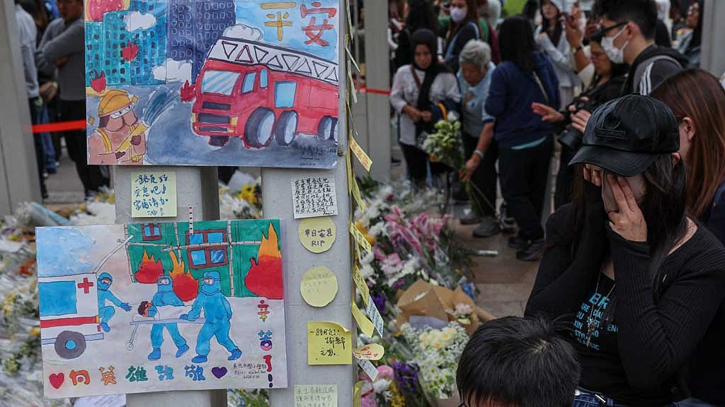 A woman wipes her eyes at a makeshift memorial at Wang Fuk Court housing complex to pay tribute to victims, following a deadly fire, in Tai Po, Hong Kong, China, Nov 30, 2025. REUTERS/Tyrone Siu