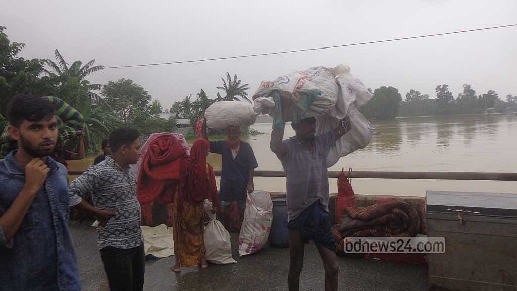 ঘরে গলা সমান পানি হওয়ায় শনিবার সন্ধ্যায় নিরাপদ আশ্রয়ের সন্ধানে যাচ্ছেন নালিতাবাড়ীর নাকশি গ্রামের এক পরিবার। 
